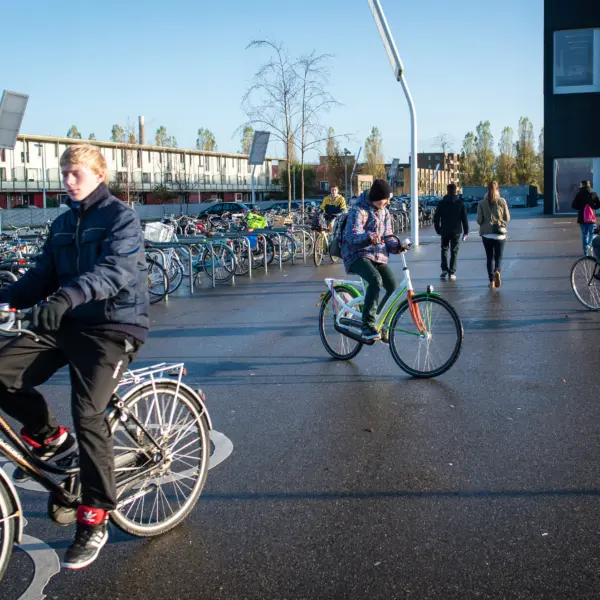 Fietsers en voetgangers maken gebruik van een openbare ruimte met fietsenstallingen en woongebouwen in een stedelijke omgeving.